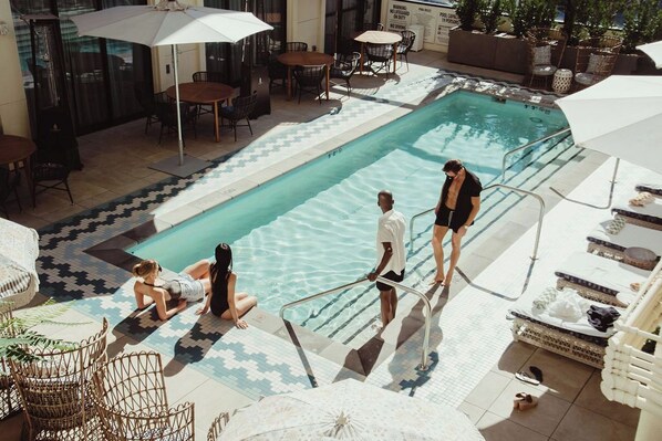 Zona de piscina con sillones reclinables, una mesa junto a la piscina y una terraza con baldosas.