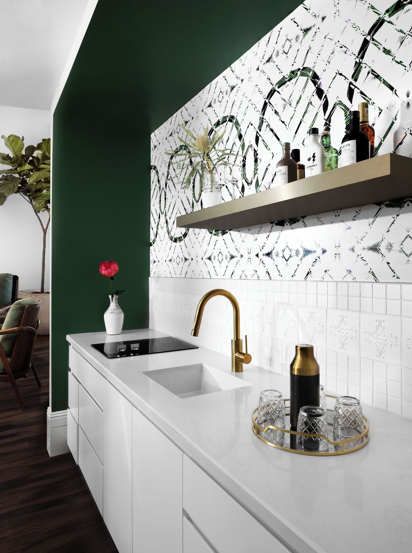 A modern kitchen with a white countertop, a gold faucet, and a decorative tray with glasses.