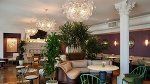 Amplia sala de estar con sofá modular, mesas redondas, sillas verdes y plantas decorativas.