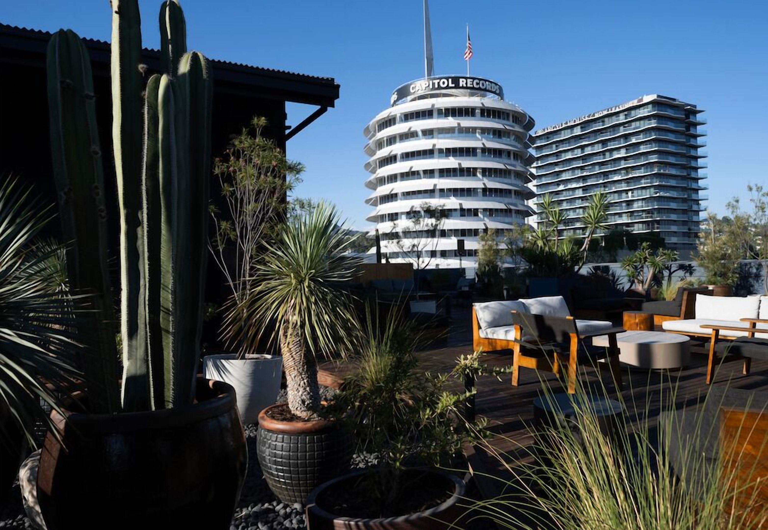 A hotel with a circular building labeled 'Capitol Records,' outdoor seating with chairs and tables, and cacti in the foreground.