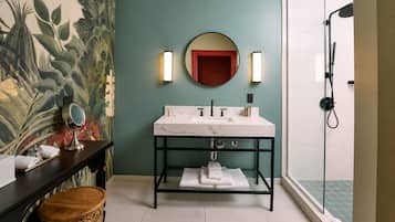 A bathroom with a marble sink, a round mirror, a shower, and a decorative wall.