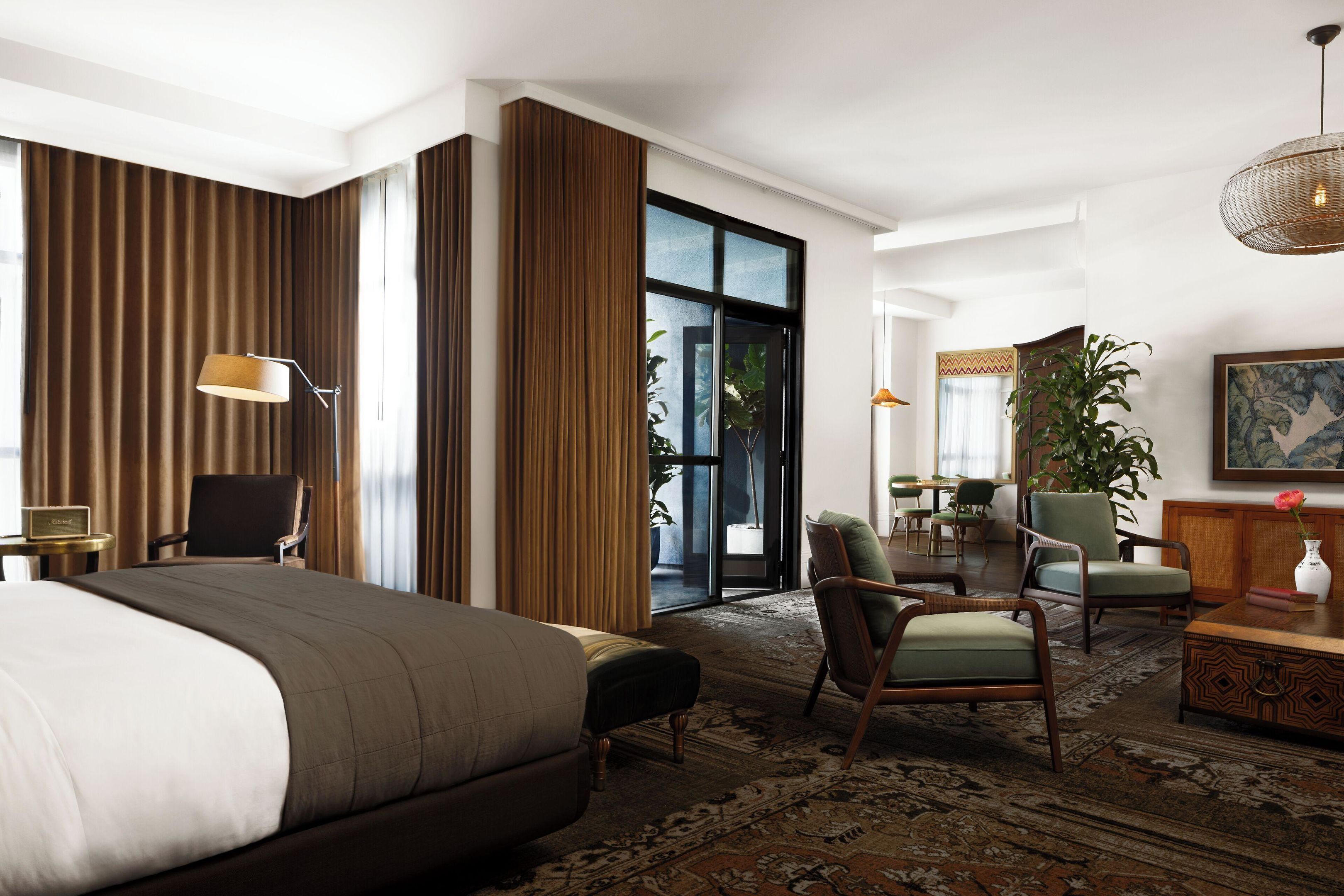 Quarto de hotel com uma cama grande, uma escrivaninha, uma cadeira, um sofá, área de refeições e uma janela ampla.