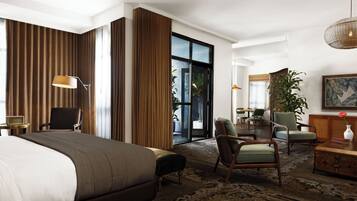 Quarto de hotel com uma cama grande, uma escrivaninha, uma cadeira, um sofá, área de refeições e uma janela ampla.