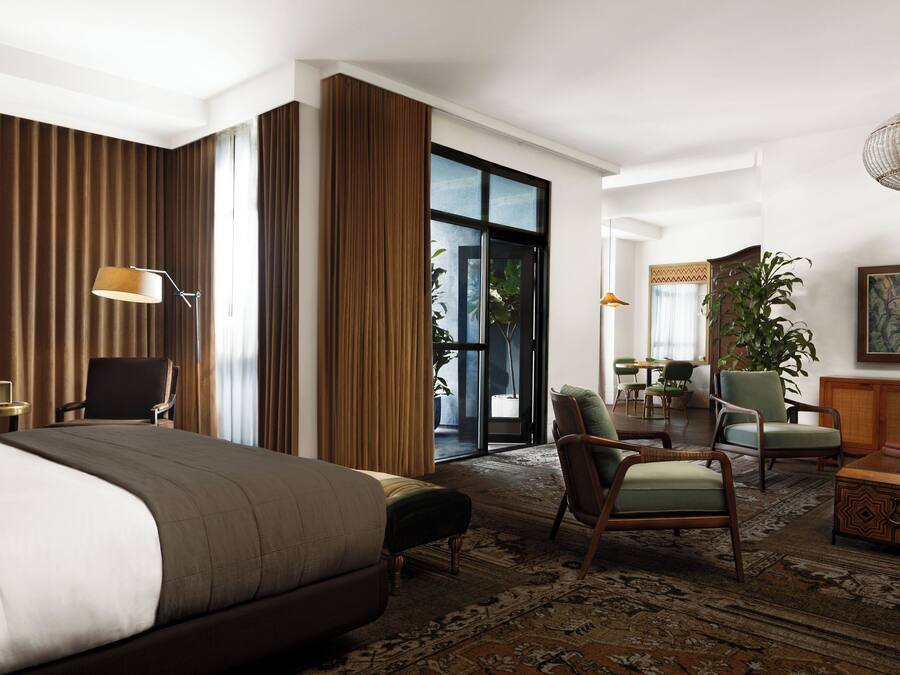 Quarto de hotel com uma cama grande, uma escrivaninha, uma cadeira, um sofá, área de refeições e uma janela ampla.
