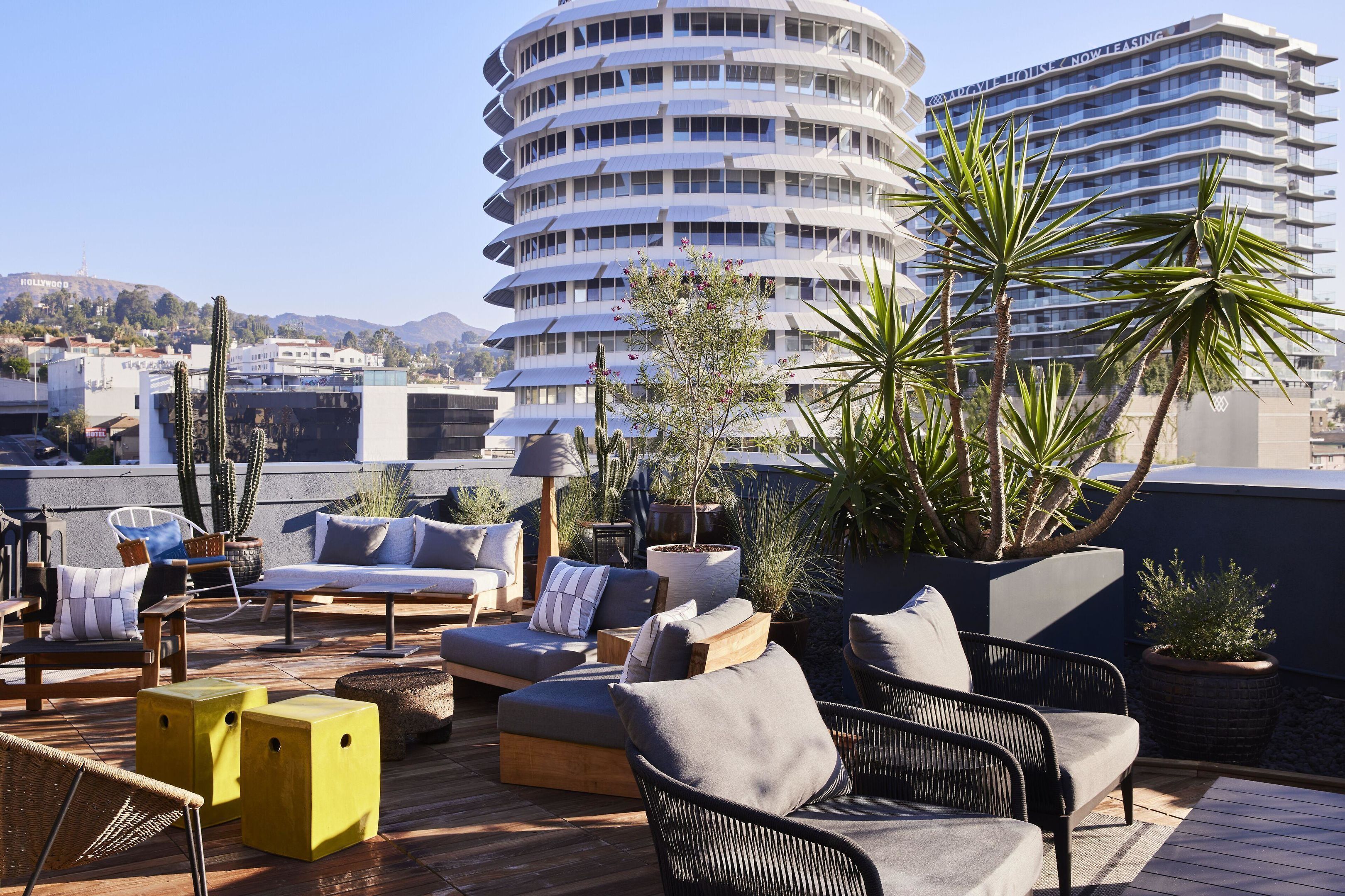 A rooftop terrace with outdoor seating, potted plants, and a view of a multi-story building with a sign.