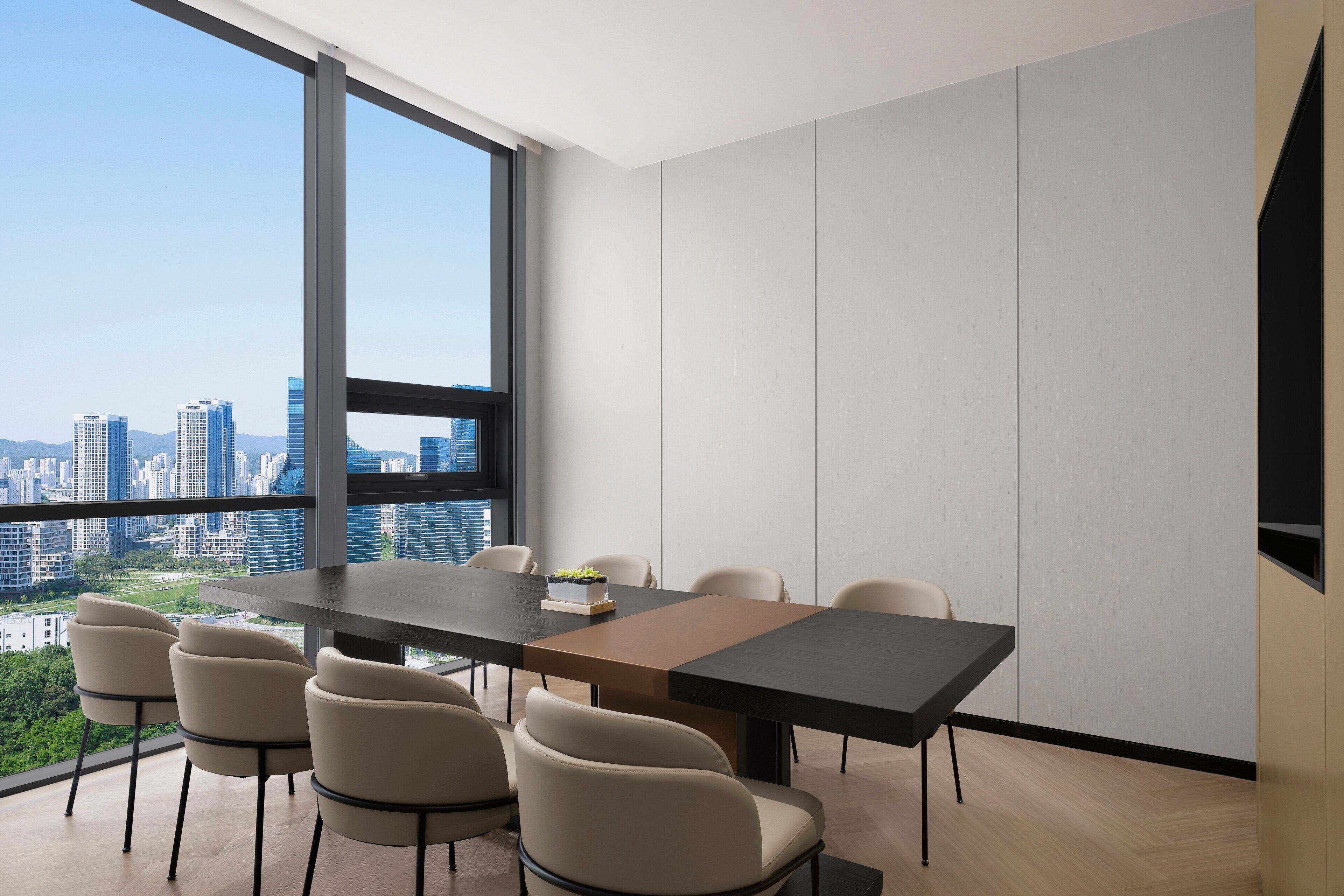 A modern dining area with a large table and chairs, large windows offering a city view, and a minimalist interior design.