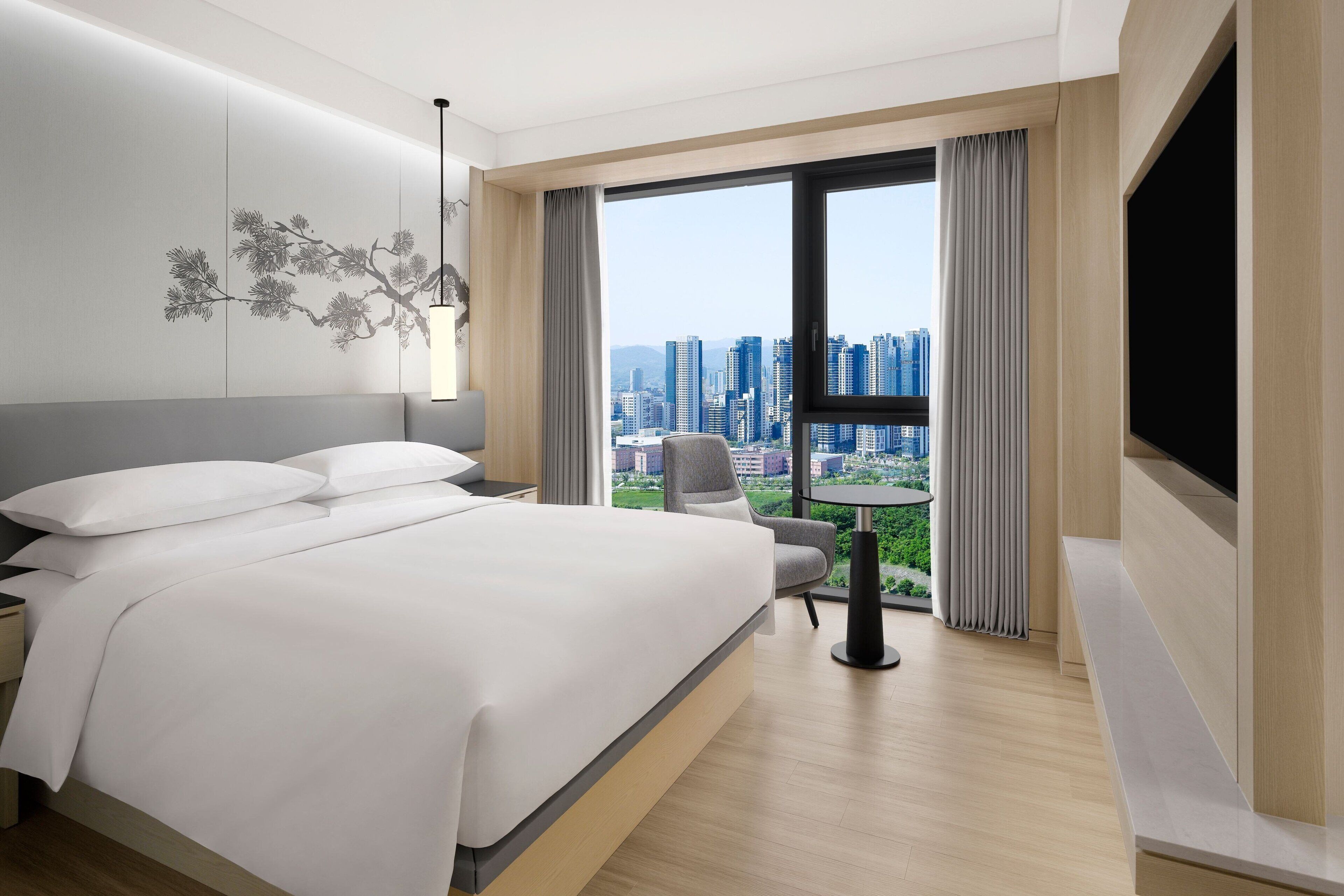 A modern hotel room with a large bed, a desk, a chair, and a TV.