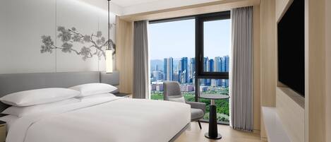 A modern hotel room with a large bed, a desk, a chair, and a TV.