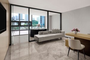 Una sala de estar moderna con un sofá, una mesa de comedor preparada para dos personas y vistas de la ciudad a través de grandes ventanales.