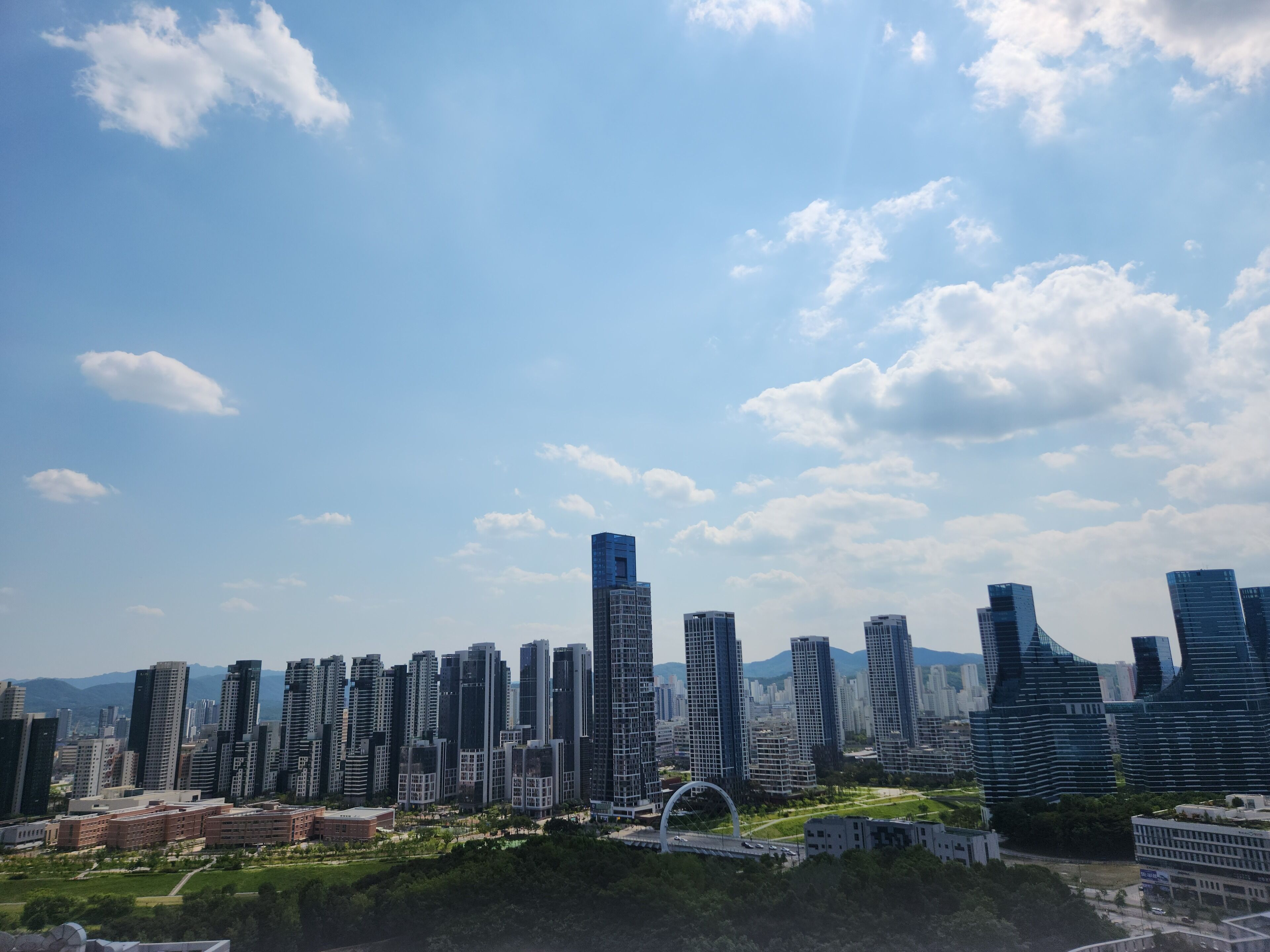 A cityscape with modern high-rise buildings, a bridge, and a park area.