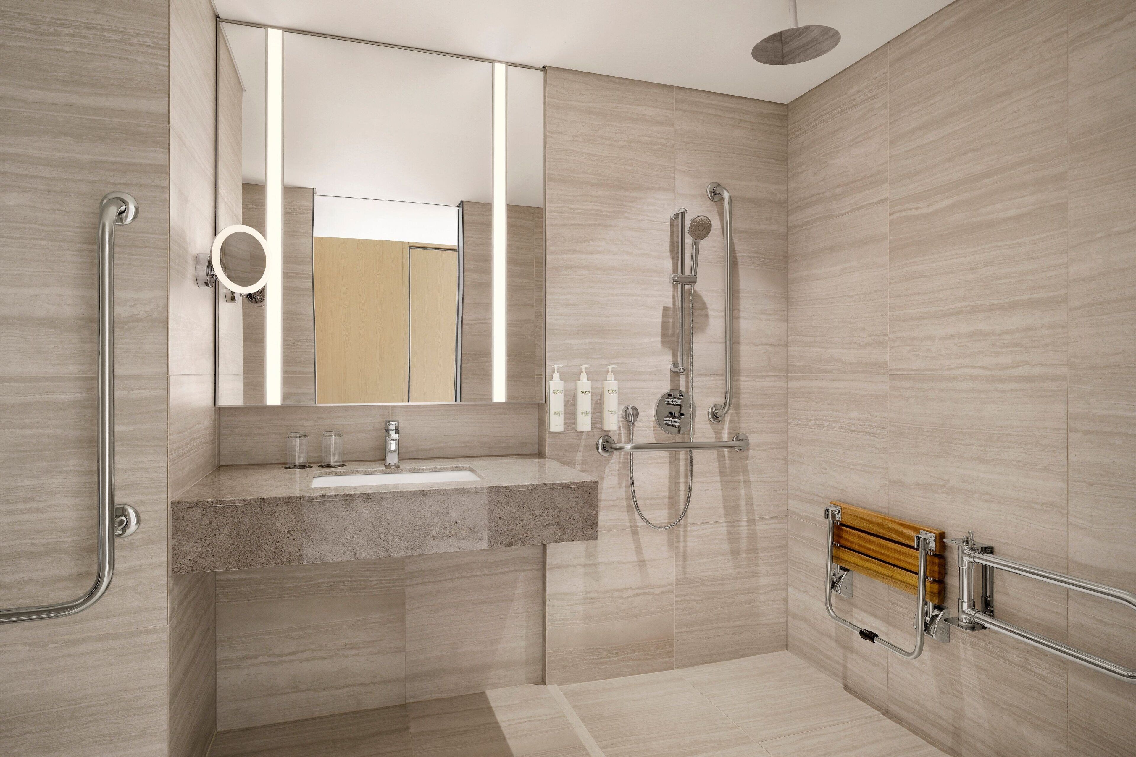 A modern bathroom with a granite sink, a handheld showerhead, and a wooden bath bench.