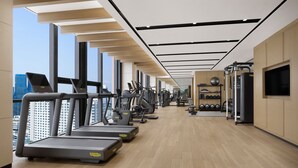 Une salle de sport moderne équipée de tapis de course, de vélos elliptiques et de poids libres, avec de grandes fenêtres et un plafond haut.