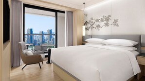 Une chambre d’hôtel moderne, dotée d’un grand lit, d’une chaise, d’une table de chevet et offrant une vue sur les toits de la ville grâce à de grandes fenêtres.