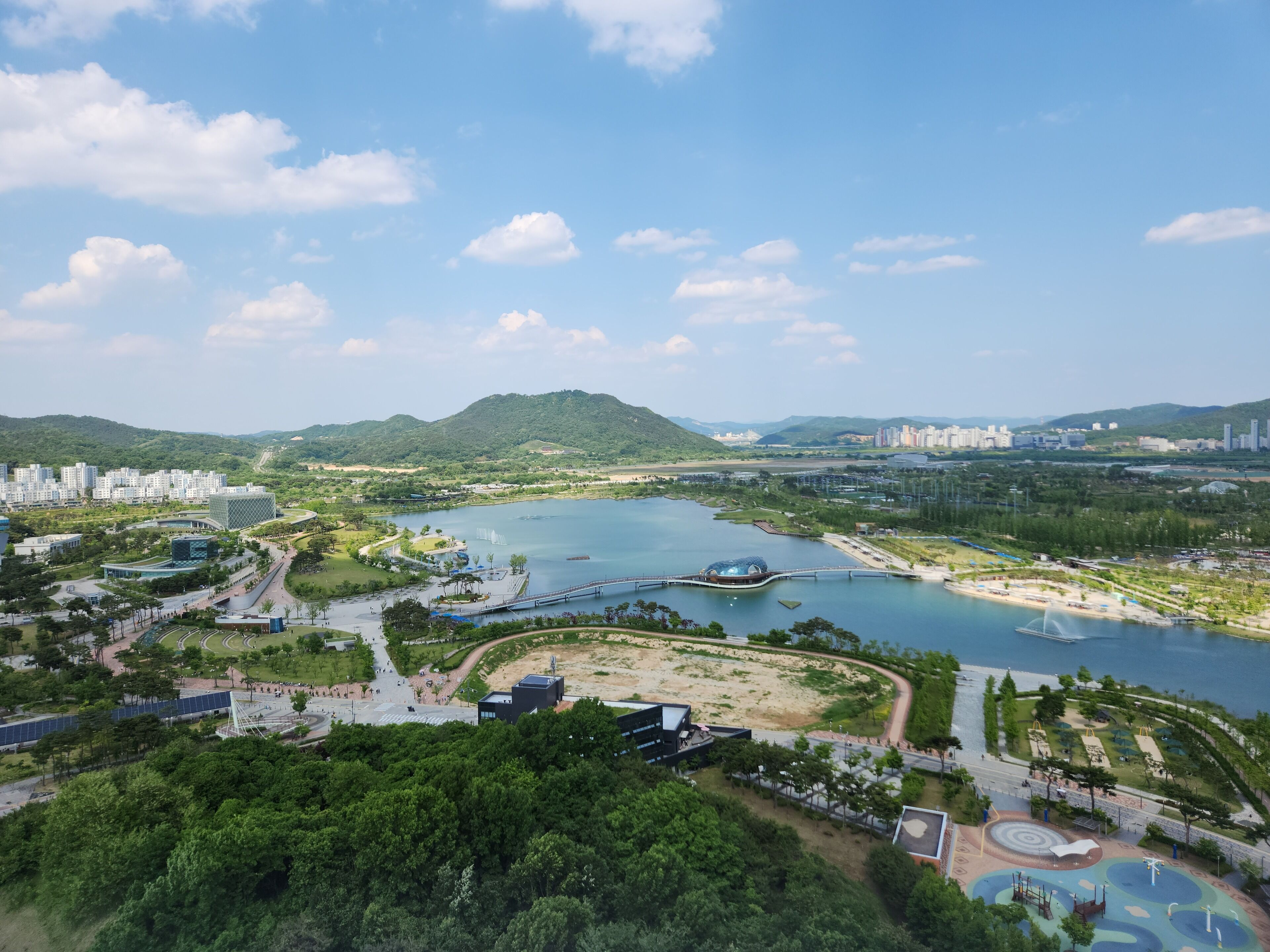 Vista panorámica de una ciudad costera con un río, un puente y un parque con áreas de juegos.