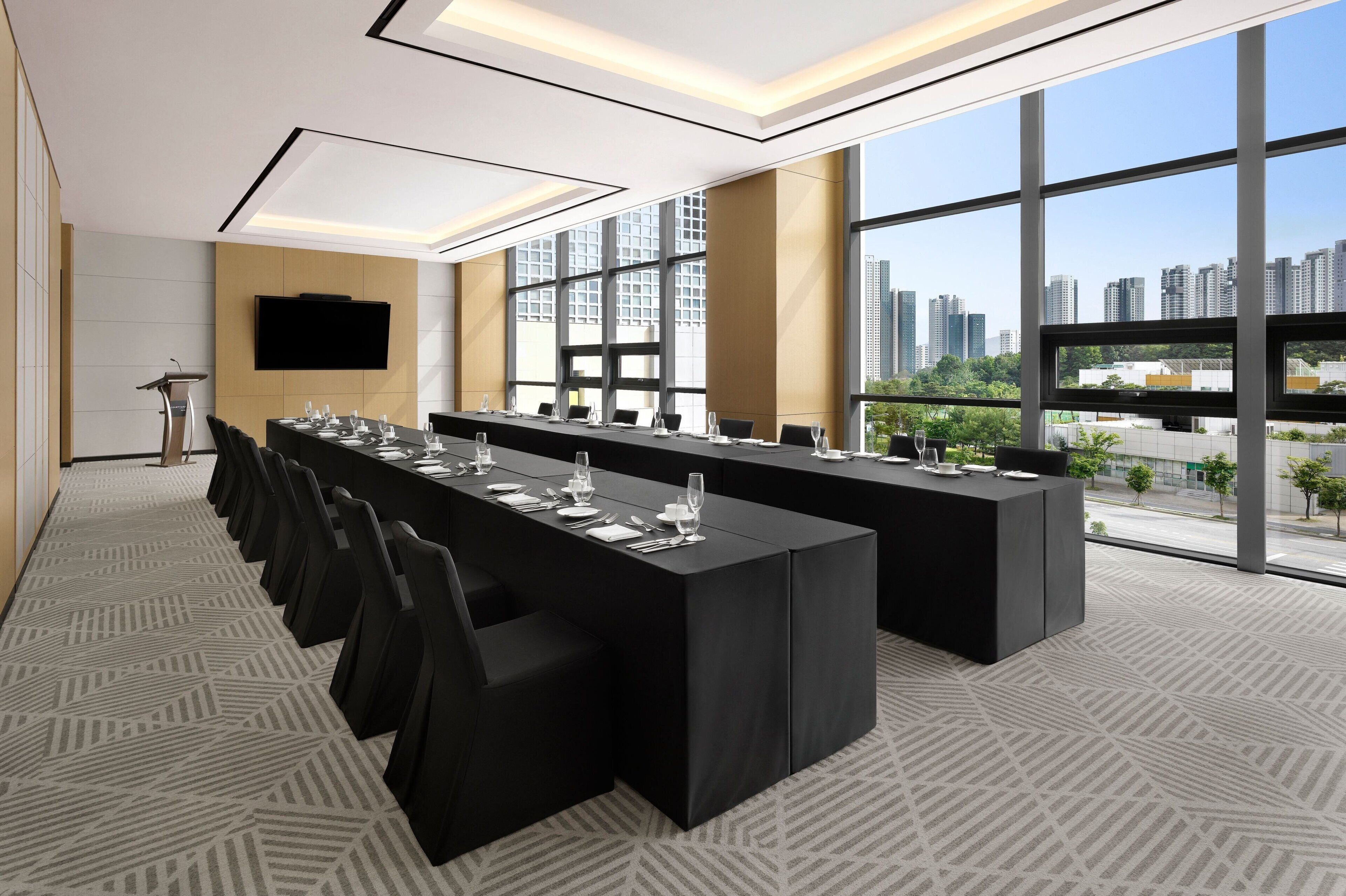 Un salón de conferencias con mesas largas, sillas, un atril y un ventanal con vista a la ciudad.
