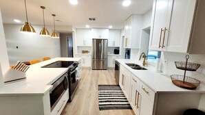 A modern kitchen with white cabinetry, stainless steel appliances, and pendant lighting.