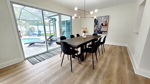 A dining area with a large table, black chairs, and a view of a swimming pool through glass doors.