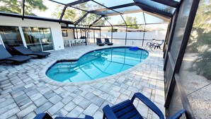 A swimming pool with a curved edge, surrounded by lounge chairs and a covered patio area.