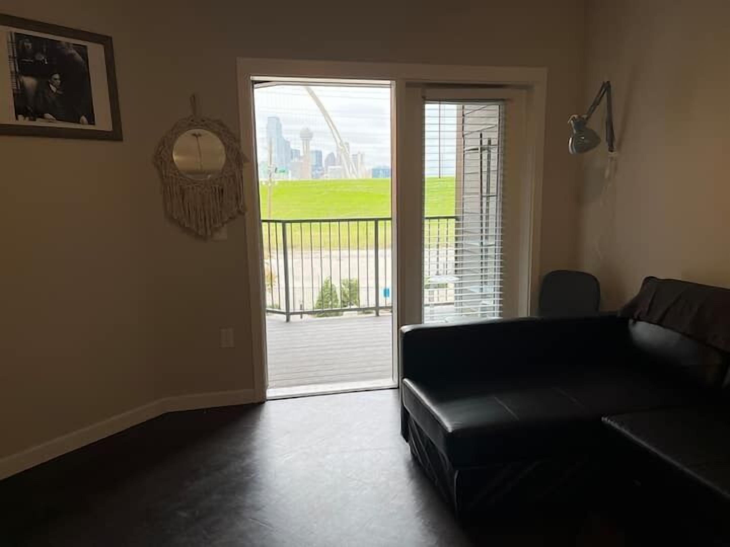 A living room with a black leather sofa, a framed picture on the wall, and a view of a cityscape through a glass door.