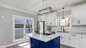 A modern kitchen with white cabinets, a blue island, stainless steel appliances, and a large window offering a view. - Tranquil waterfront getaway (Ashland City)