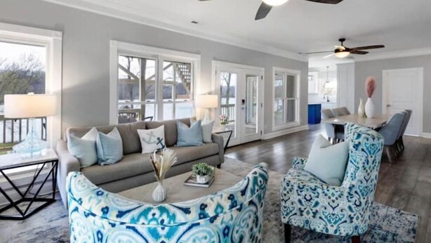 A spacious living room with a sofa, armchairs, and a coffee table. There are ceiling fans, large windows, and a dining area in the background. - Tranquil waterfront getaway (Ashland City)