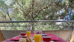 A table set with breakfast items, including bread, a glass of orange juice, and red cups, on a balcony with a view of trees. - Apartment Vedrana - great value near beach and free parking (Dubrovnik)
