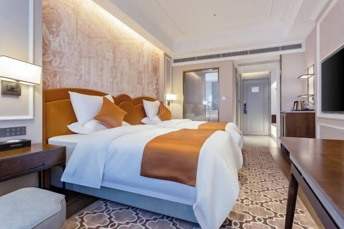 Ein Hotelzimmer mit einem großen Bett, Nachttischen, einem Fernseher und einem gemusterten Teppich.