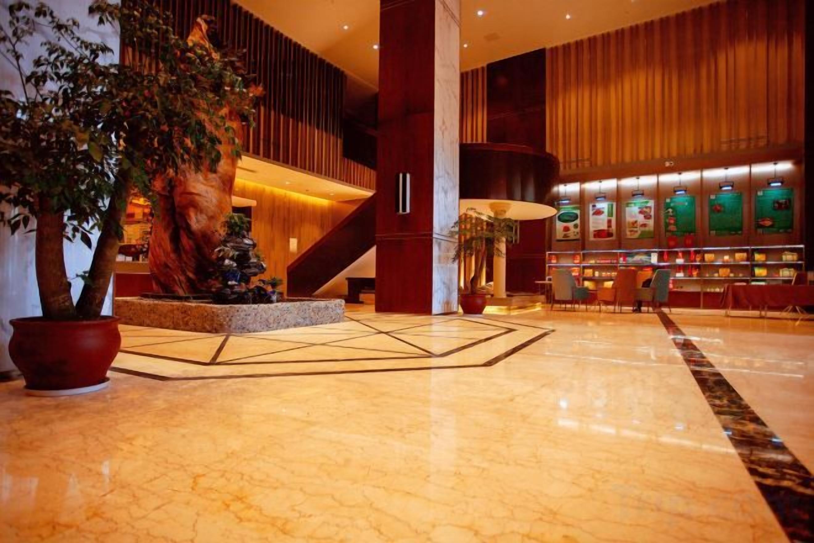A lobby with a marble floor, a large tree, a staircase, and a reception desk.