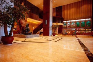 A lobby with a marble floor, a large tree, a staircase, and a reception desk.