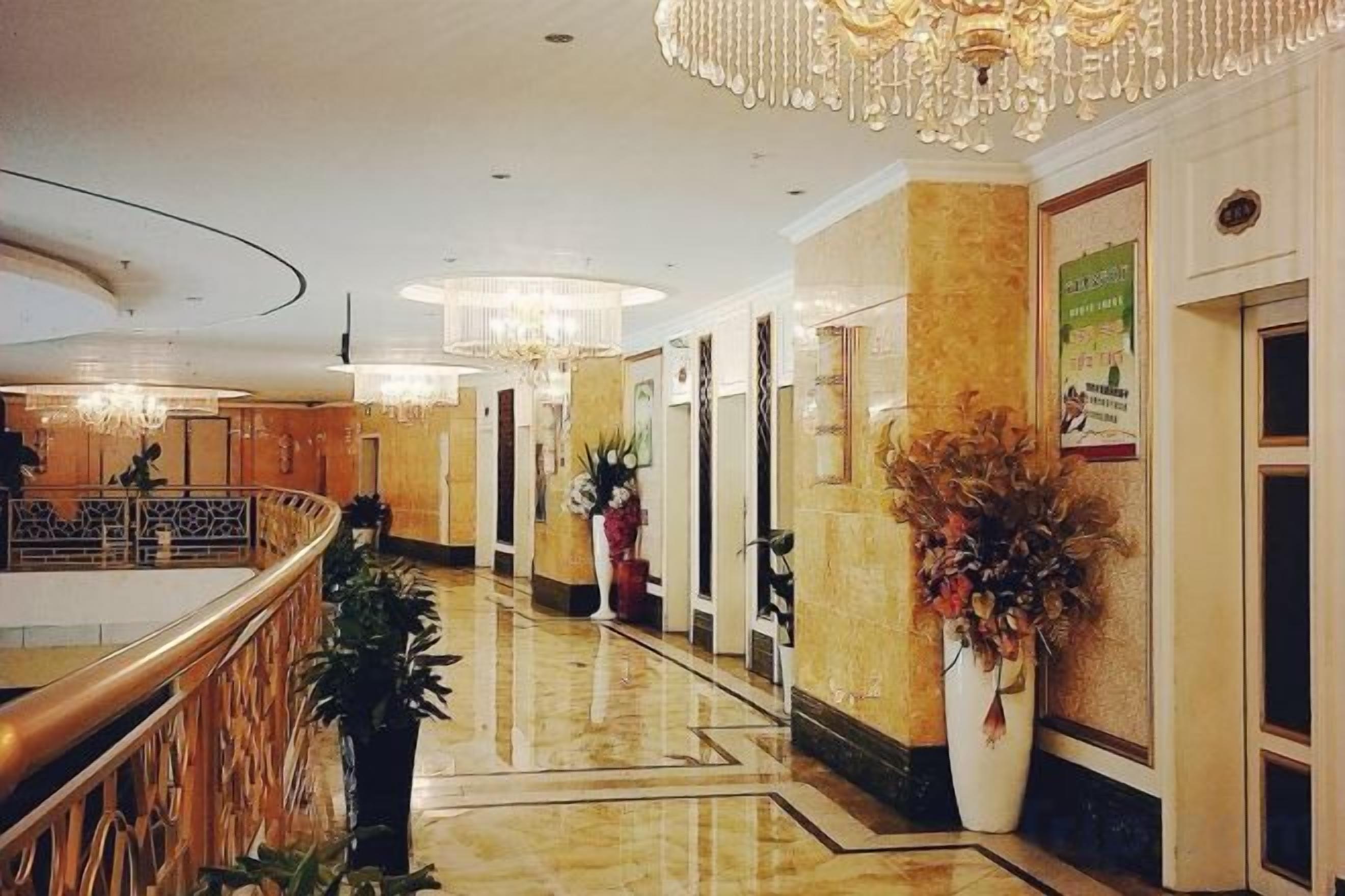 A hotel lobby with a marble floor, a reception desk, and a large potted plant.