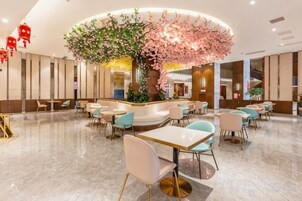 Un hall de hotel con una zona de estar central, una recepción y un árbol decorativo grande.