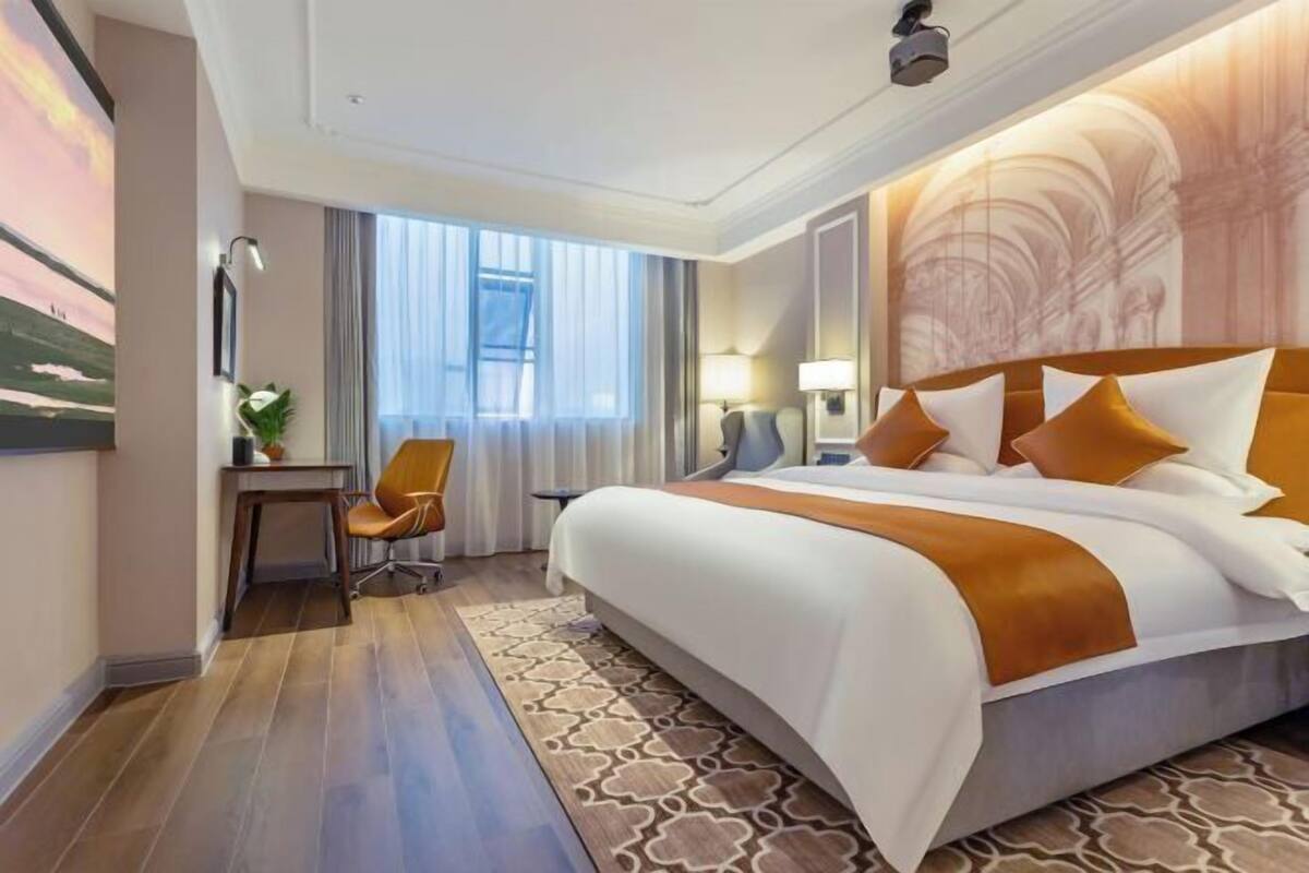 Ein Hotelzimmer mit einem großen Bett, einem Schreibtisch, einem Stuhl und einem Fenster mit Vorhängen.
