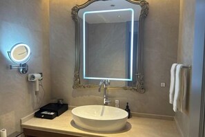 A bathroom with a round mirror, a rectangular mirror with a neon light, a white sink, and a towel rack. - Sheng Shi Jin Hai Grand Hotel (Nayong)