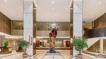 A modern lobby with marble columns, a central sculpture, and potted plants.