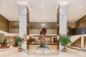 Un lobby moderno con columnas de mármol, una escultura central y plantas en macetas.
