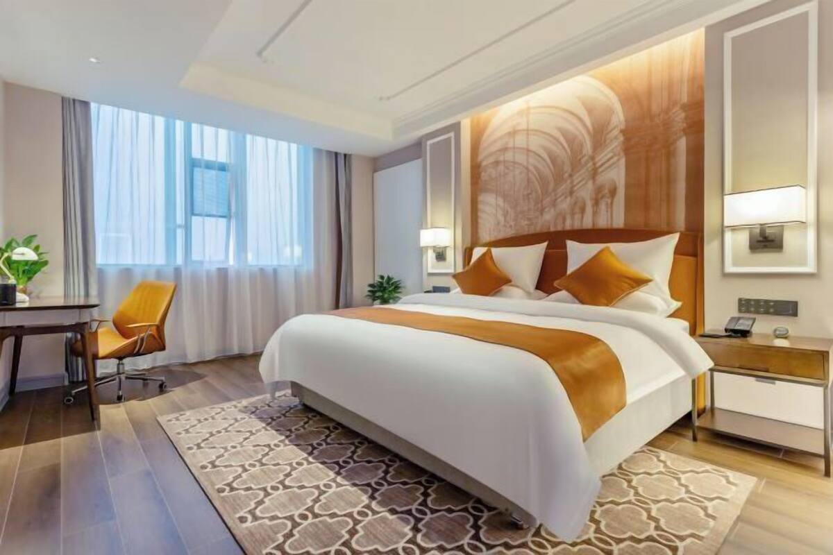 Ein Hotelzimmer mit einem großen Bett, einem Schreibtisch, einem Sessel, einem Nachttisch und einem Fenster mit Vorhängen.