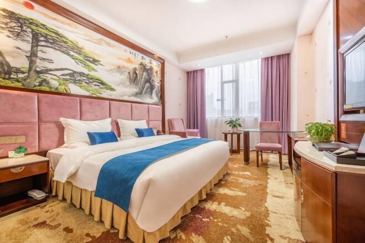 Ein Hotelzimmer mit einem großen Bett, einem Schreibtisch, einem Sessel, einem Fernseher und einem Bild an der Wand.