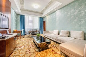 A hotel room with a sofa, a coffee table, a desk, and a TV.