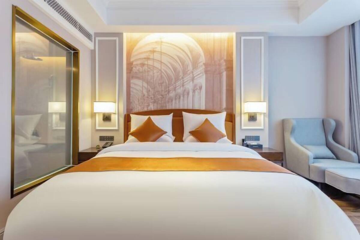 Ein Hotelzimmer mit einem großen Bett, zwei Nachttischlampen, einem Sessel und einer Wand mit einem großen Wandgemälde.