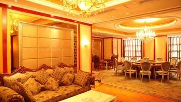 A hotel lobby with a sofa, a coffee table, a chandelier, and a dining area with chairs and a table.