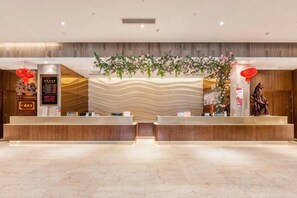 A hotel reception area with a modern design, featuring a reception desk, a digital display, and a decorative wall with plants. - Sheng Shi Jin Hai Grand Hotel (Nayong)