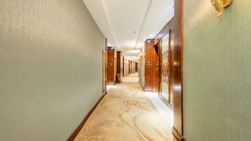 A hotel corridor with carpeted flooring, doors, and wall-mounted light fixtures.
