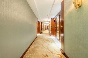 A hotel corridor with carpeted flooring, doors, and wall-mounted light fixtures.
