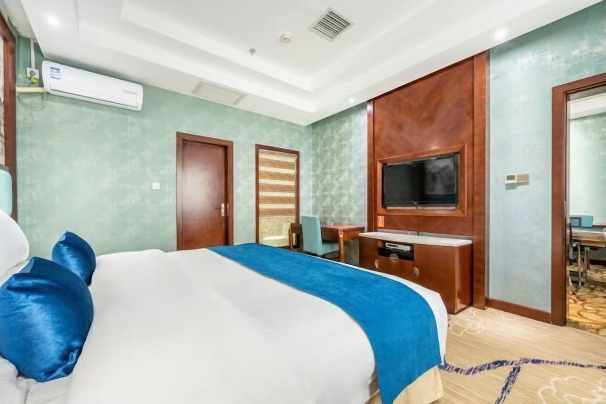 Hotellihuone, jossa on suuri sänky, seinälle asennettu televisio ja työpöytä tuolilla.