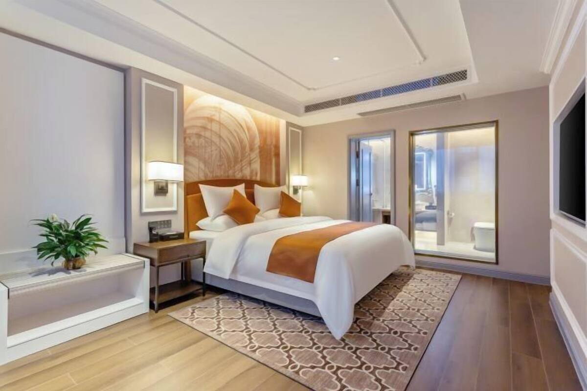 Ein Hotelzimmer mit Bett, Nachttischen, einer Lampe, einer Pflanze und Blick ins Badezimmer.