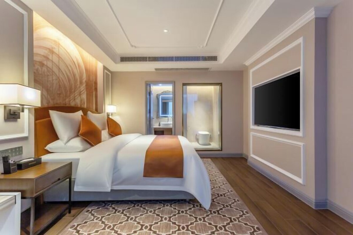 Hotellihuone, jossa on suuri sänky, yöpöydät, taulutelevisio ja kuviollinen matto.