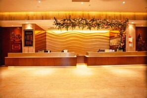 A hotel reception area with a reception desk, a digital display, and a decorative plant. - Sheng Shi Jin Hai Grand Hotel (Nayong)