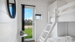 Een kamer met een stapelbed, een klein tafeltje met een bloempot, een raam met uitzicht op een groen gazon en een deur naar buiten.