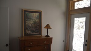 Un dormitorio con un aparador de madera, un cuadro enmarco, una lámpara y una puerta que da a un balcón.