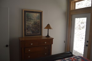 Een slaapkamer met een houten dressoir, een ingelijst schilderij, een lamp en een deur naar een balkon.